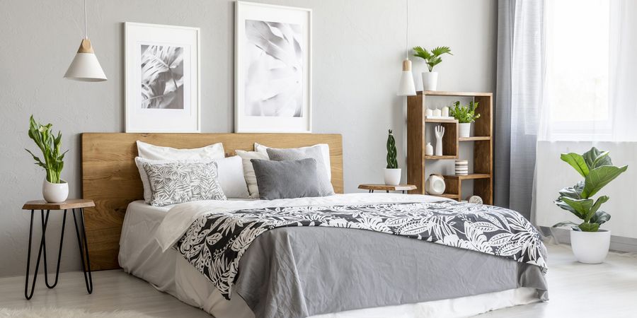 Modernes Bett mit Kopfteil aus Holz in einem freundlichen Schlafzimmer mit Zimmerpfllanzen