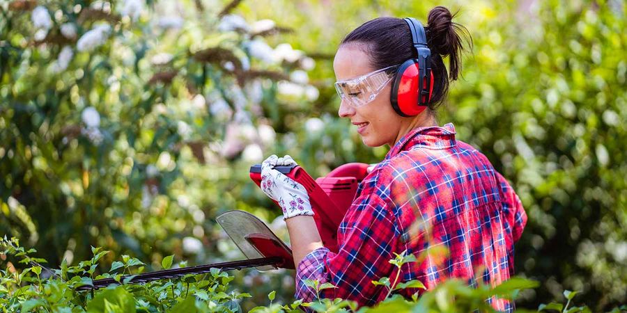 Frau mit gehörschutz schneidet im Garten die Hecke