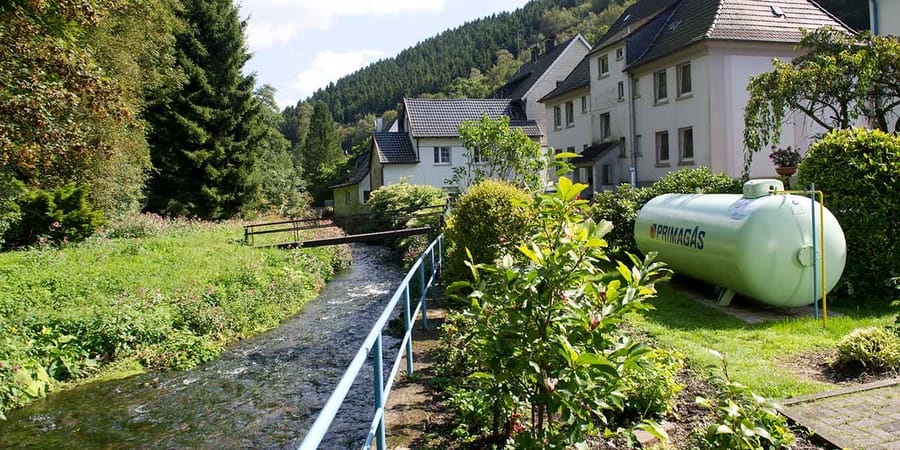 Einfamilienhaus am Fluss. Im Garten steht ein hellgrüner Flüssiggas-Tank von Primagas