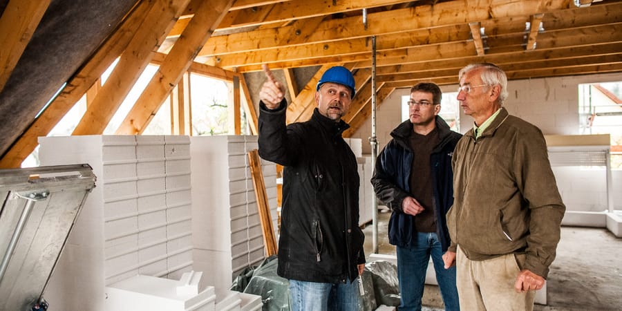 Experte prüft Dachkonstruktion mit beiden Bauherren im Rohbau