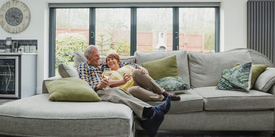 Ein älteres Ehepaar lächelt sich zufrieden auf einer Couch an.