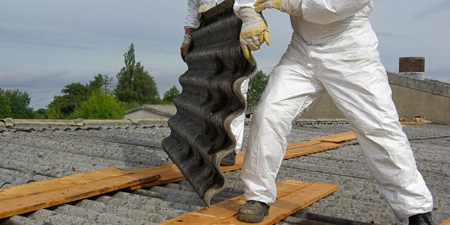 Handwerker entfernt mit Schutzkleidung asbesthaltige Dachplatten.
