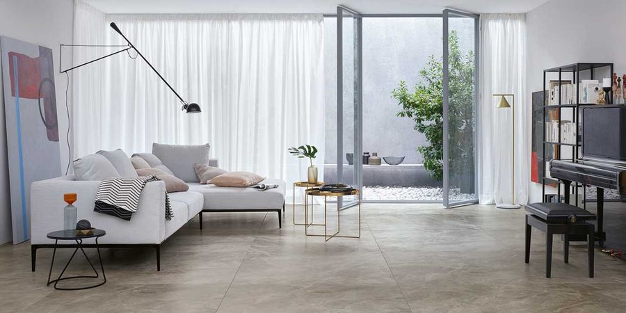 Natursteinfliese in Wohnzimmer mit großer Fensterfront und hellem Sofa
