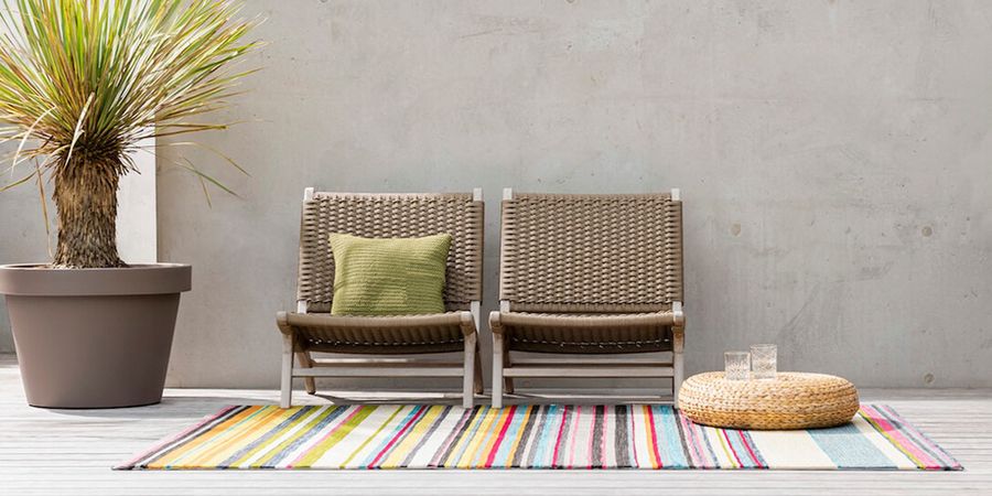 Stühle auf einem Outdoor-Teppich auf einem kleinen Balkon.