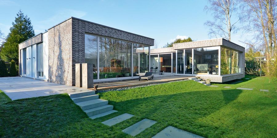 Luxus Bungalow in C-Form vom Architekten frei geplant. Die Fassade ist mit grauen Klinkersteinen gestaltet. Das Dach ist ein Flachdach. Im Innenhof befindet sich eine geschützte Terrasse mit Zugang zum Garten.