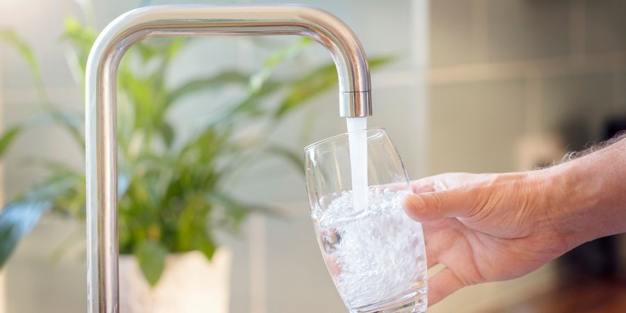 Leitungswassert fließt in ein Glas aus Wasserhahn in Küche.