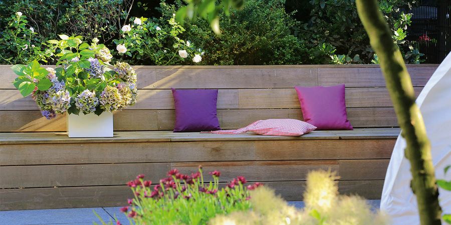 Garten mit Sitzbank und lila Outdoor Kissen.