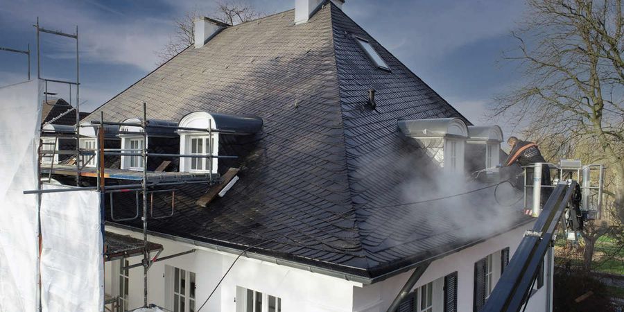 professionelle Dachreinigung: Die Dachdecker reinigen das Dach von Gerüsten und Schwebekörben aus.