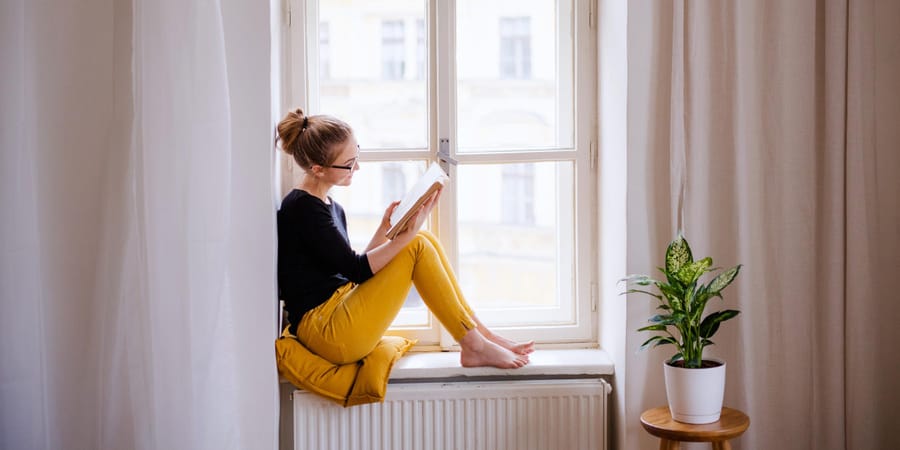 Frau auf Fensterbank mit Buch in der Hand