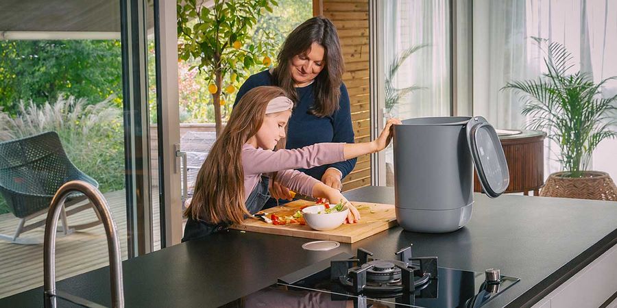 Frau und Kind befüllen kleinen Kompost-Eimer