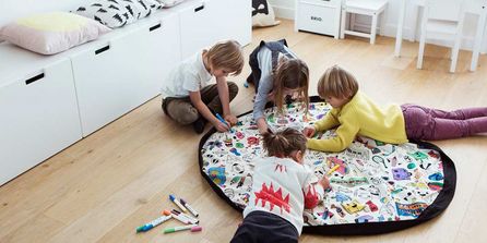 Kinder spielen auf einem Stoffteppich, der sich als Aufbewahrungsbeutel nutzen lässt.