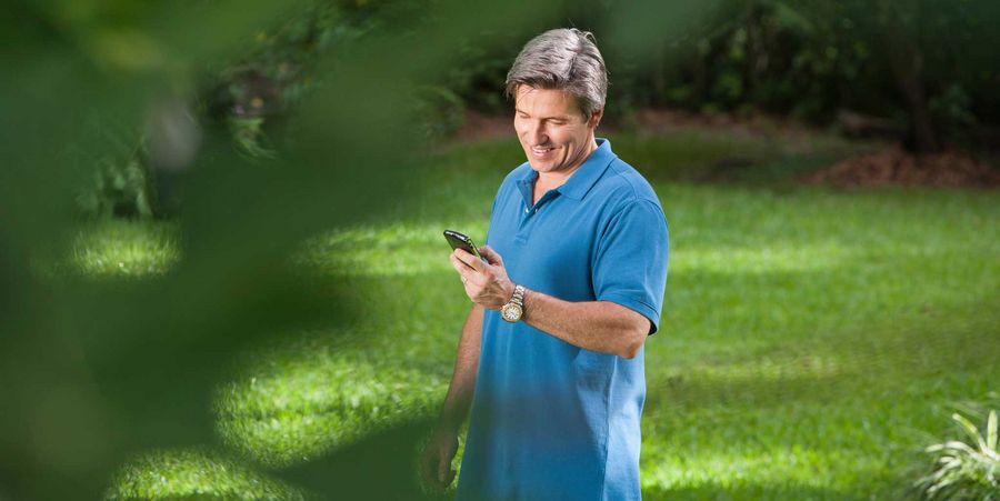 Mann im Garten mit Smartphone.