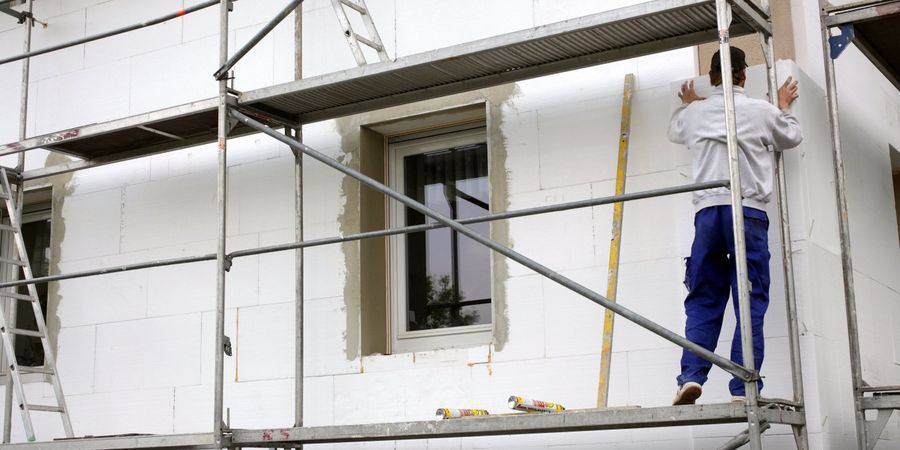 Mann dämmt im Rahmen einer energetischen Sanierung die Außenhülle eines Hauses.