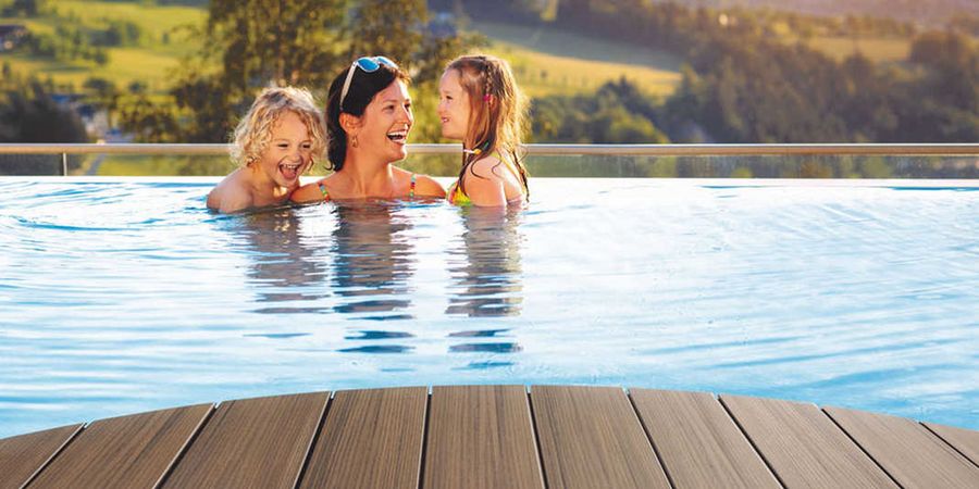 Frau mit zwei Kindern in einem Pool mit Poolumrandung aus Holz.