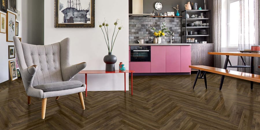 Vinylboden in dunkler Holzoptik in Fischgrätverlegung in Kombination mit hellen Wänden und pinker Küche