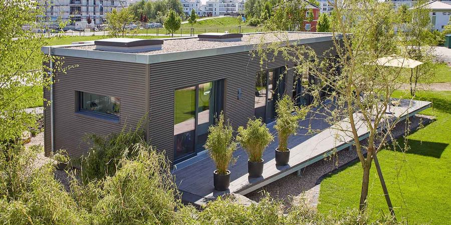 Außenansicht des Mini Bungalows mit 50 qm von Schwörer Haus. Der Grundriss ist rechteckig. Die Fassade mit Holz verschalt und drumherum ist viel Grün. 