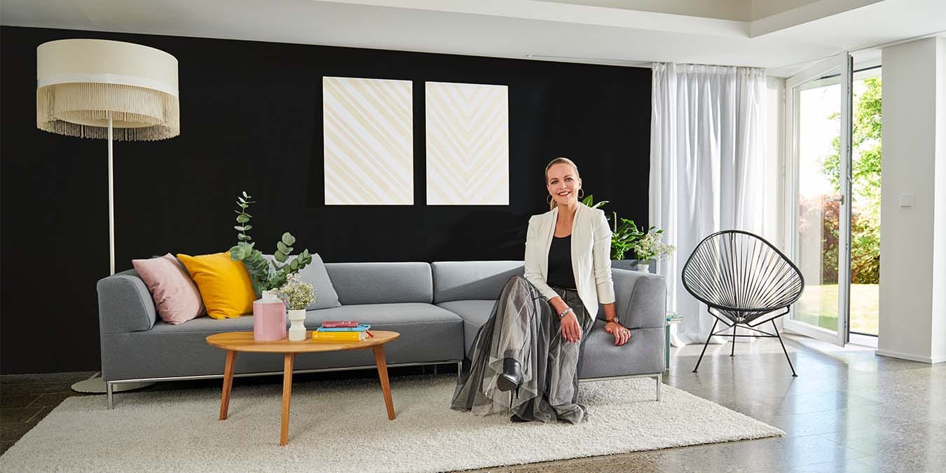 TV-Innenarchitektin Eva Brenner auf einem Sofa in einem Wohnzimmer mit schwarzer Wand.