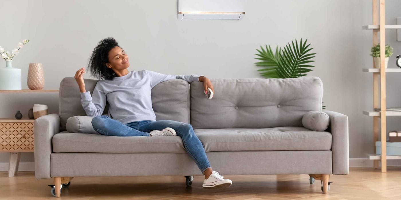 Frau auf einem Sofa steuert die Klimaanlage in der Wohnung.