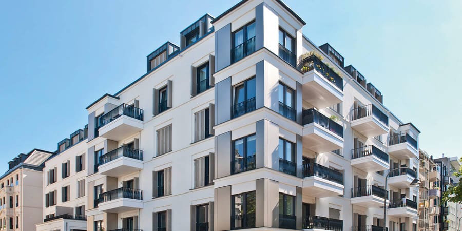Modernes Wohngebäude in Köln mit Kragarmbalkonen. Die weißen Balkone sind mit schwarzen Geländern ausgestattet und fügen sich harmonisch in das Gesamtbild mit bodentiefen Fenstern ein. 
