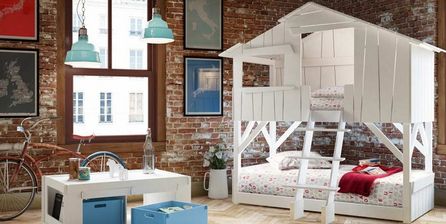 Kinderbett mit Matratze und Kissen in einem kleinen Holzhaus in einem Innenraum.