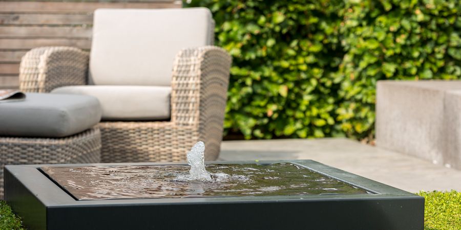 Wasserspiel auf einer Terrasse mit Outdoor-Sessel im Hintergrund.
