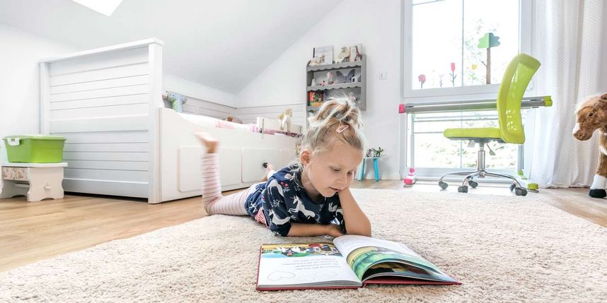 Kind liest ein Buch in wohngesundem Kinderzimmer.
