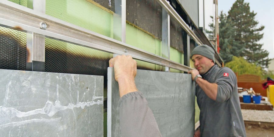 Zwei Handwerker befestigen Schieferplatten an der vorgehängten Fassade.